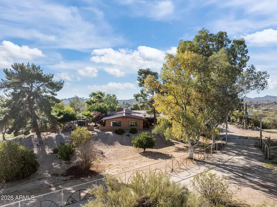 The ranch house among mature trees, desert hills beyond