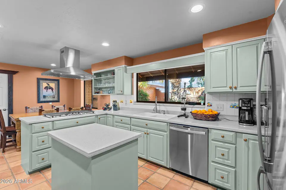 Kitchen with sage-green cabinetry, center island, and stainless hood